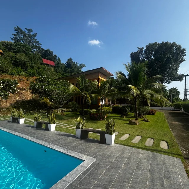 Swimming pool and manicured tropical garden with the villa beyond under blue sky