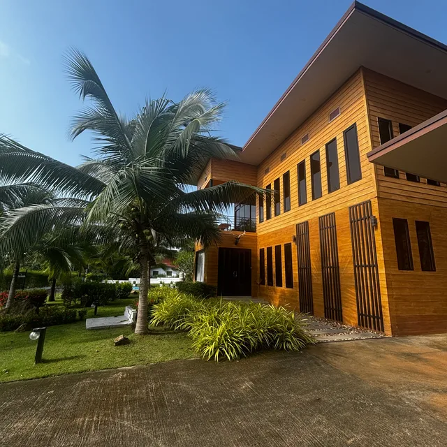 Two-storey timber villa facade with palm trees and tropical landscaping