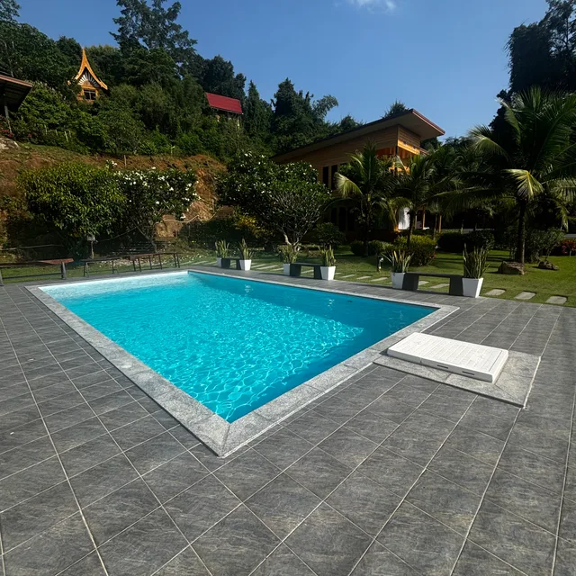 Rectangular private swimming pool with grey stone deck surrounded by tropical garden
