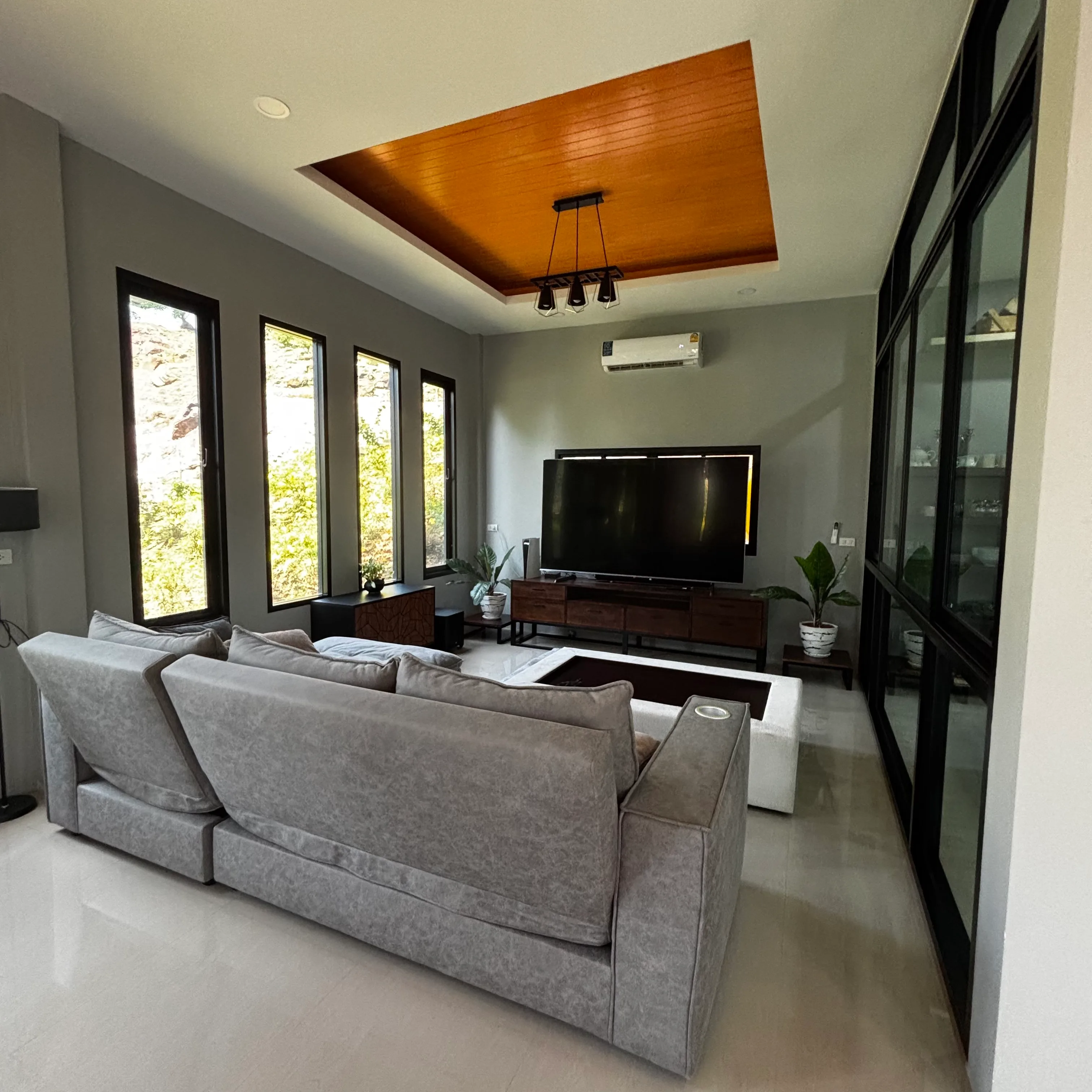 Living room with grey sectional sofa, large TV and warm wooden recessed ceiling