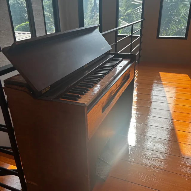 Vintage upright piano on glossy hardwood floor in front of sunlit windows