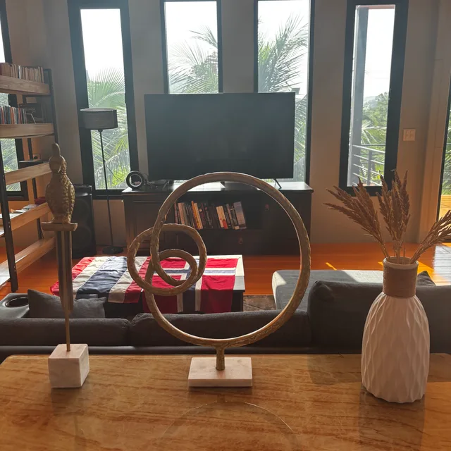 Brass sculptures and ceramic vase on a wooden console with TV lounge behind