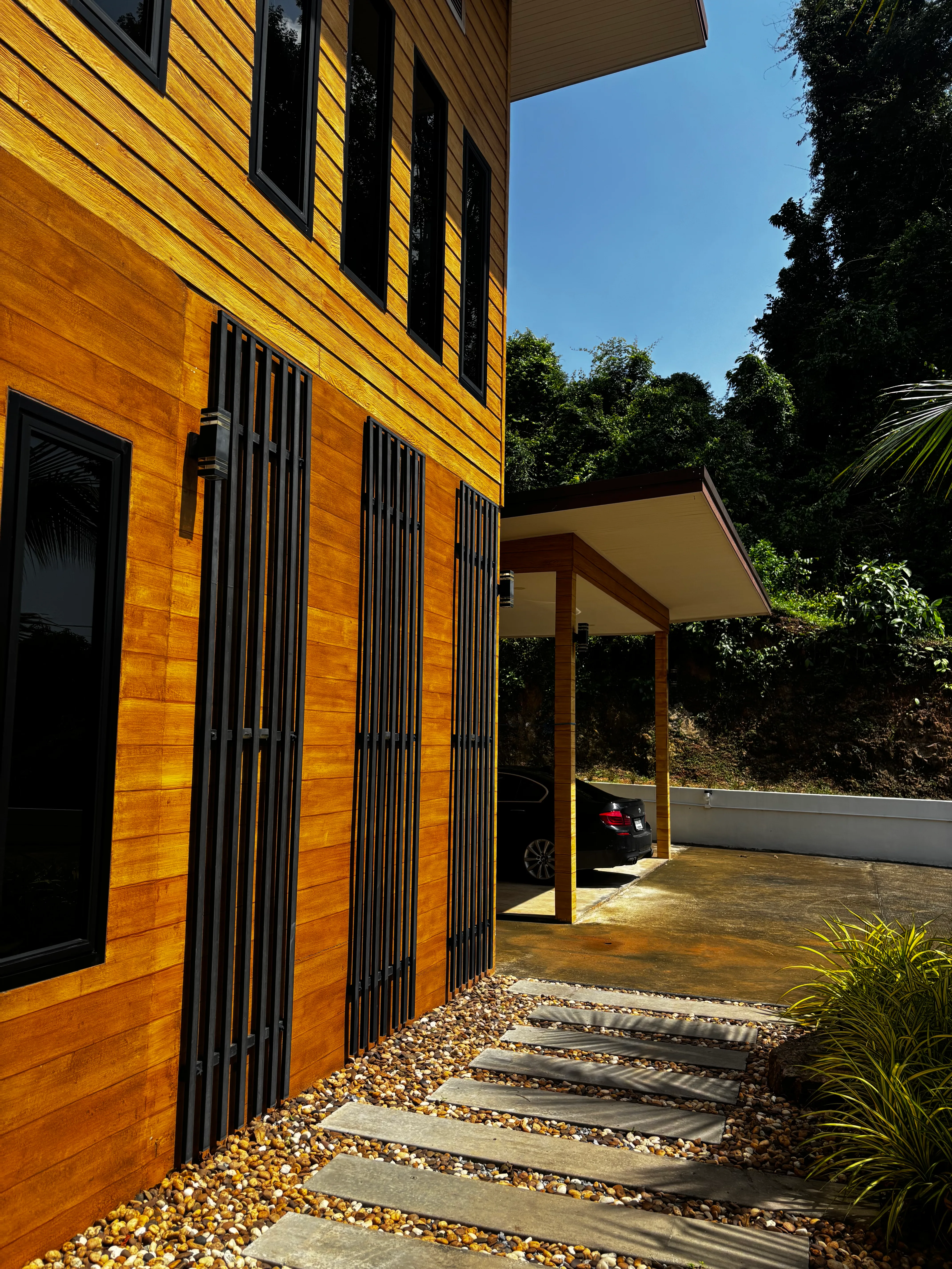 Timber-clad villa exterior with stone path and covered parking